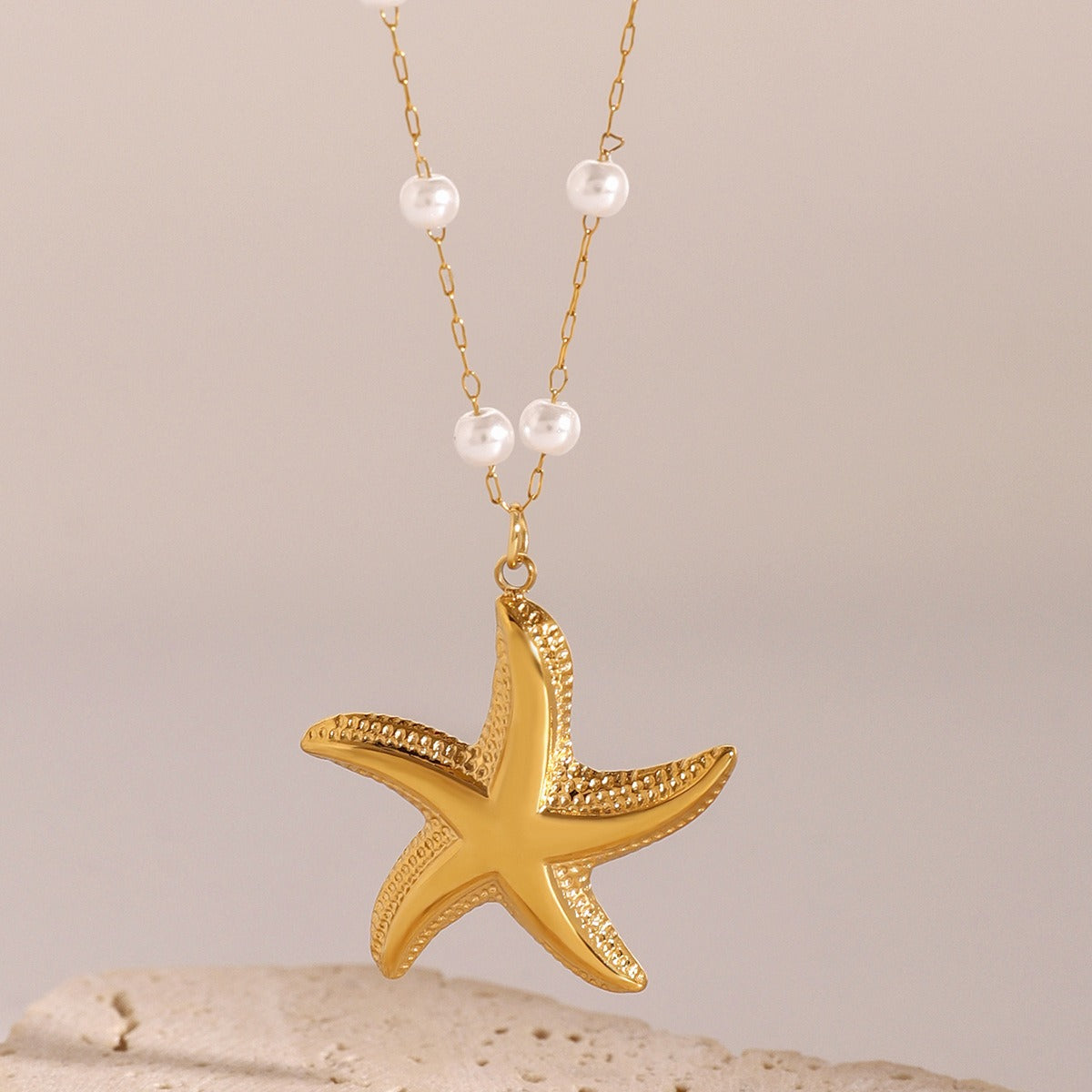 Gold starfish pendant necklace with pearls on a beige background