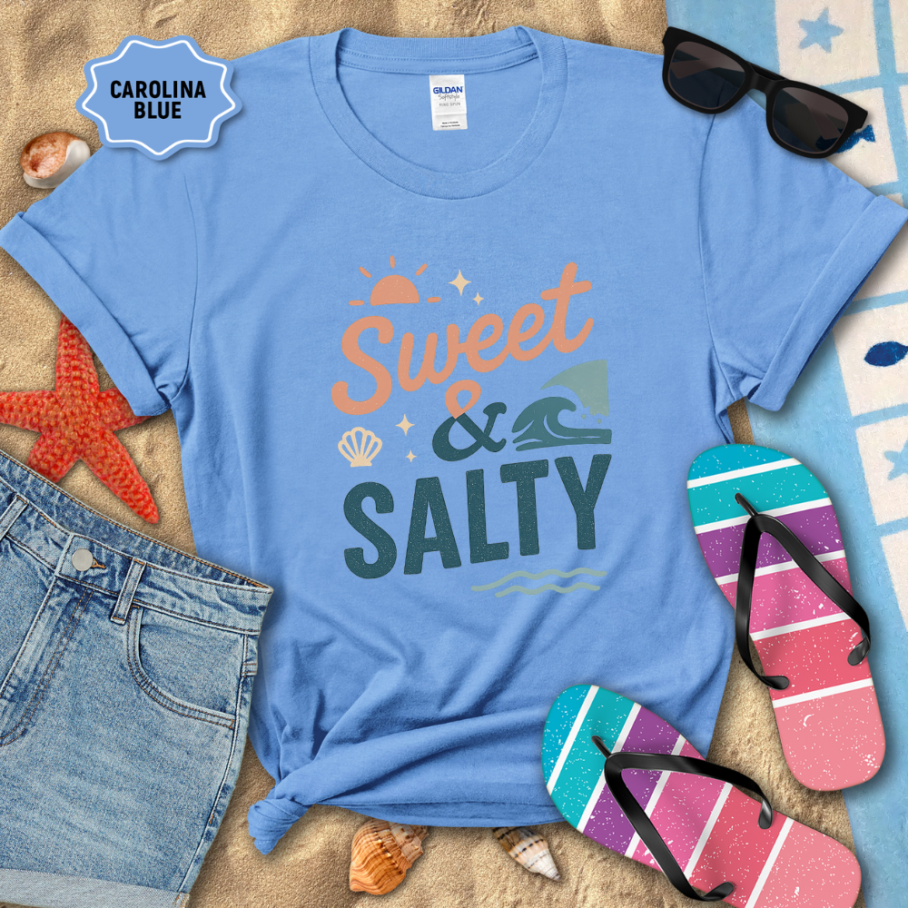 Blue t-shirt with 'Sweet & Salty' text on a sandy background with beach accessories.