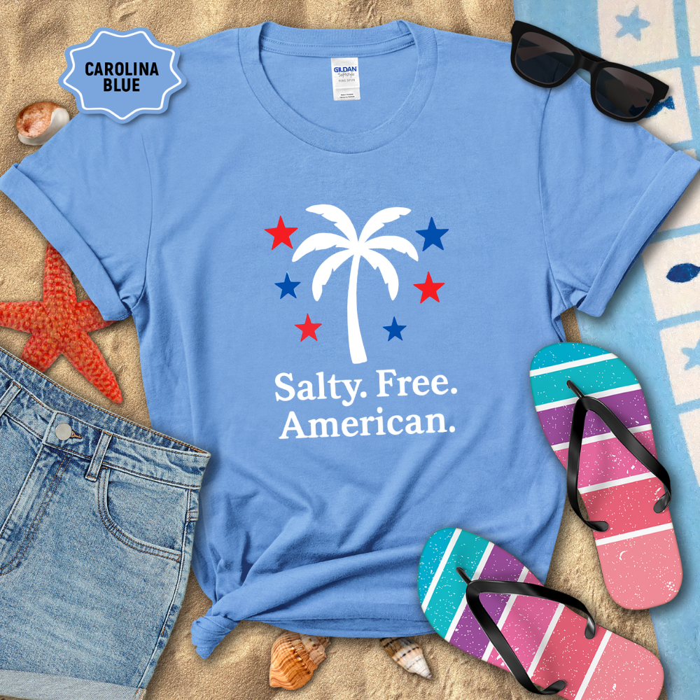 Blue t-shirt with palm tree and stars design, surrounded by beach accessories on sand.