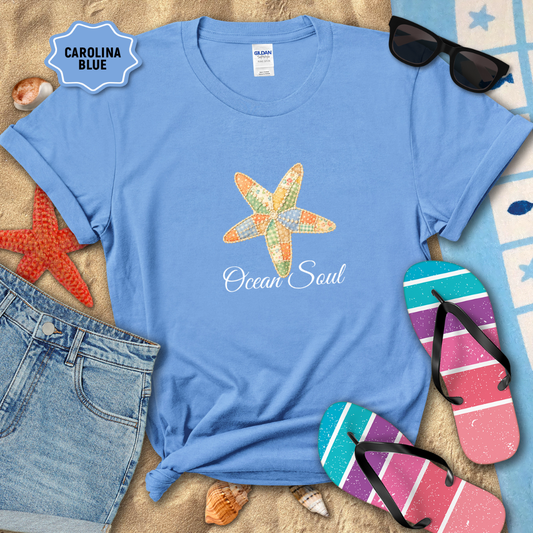 Blue t-shirt with starfish design and 'Ocean Soul' text, surrounded by beach accessories on sand.