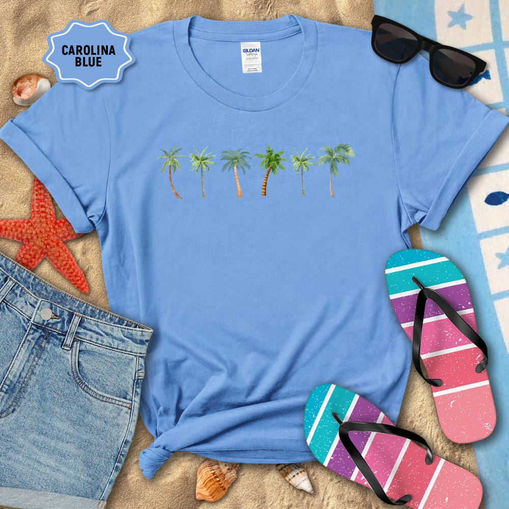 Blue t-shirt with palm tree design on a sandy background with beach accessories.