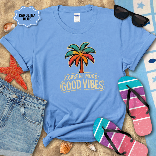 Blue t-shirt with palm tree design and 'Current Mood: Good Vibes' text, surrounded by beach accessories.