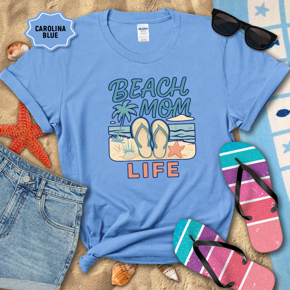Blue t-shirt with 'Beach Mom Life' design on sand with flip-flops and sunglasses.