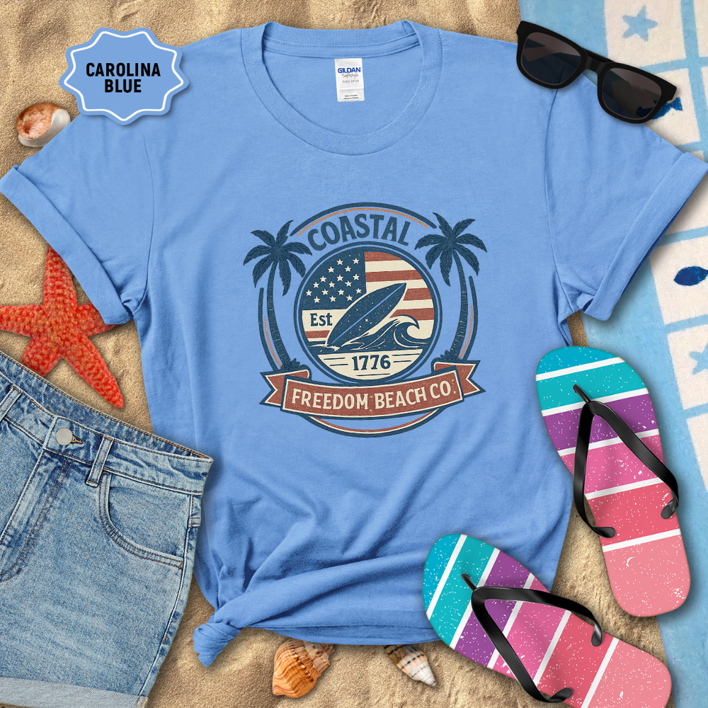 Blue t-shirt with 'Coastal Freedom Beach Co' design on sand with beach accessories.