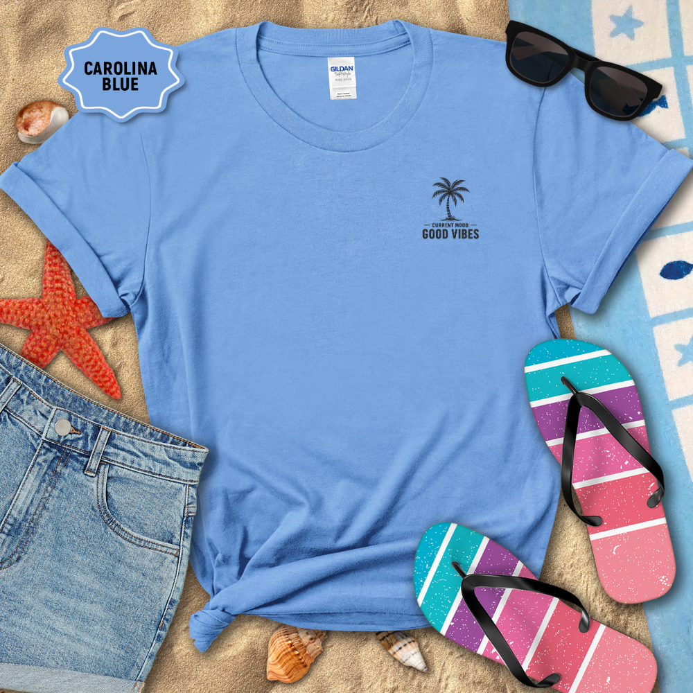 Blue t-shirt with palm tree design and 'Good Vibes' text on a sandy background with flip-flops and sunglasses.