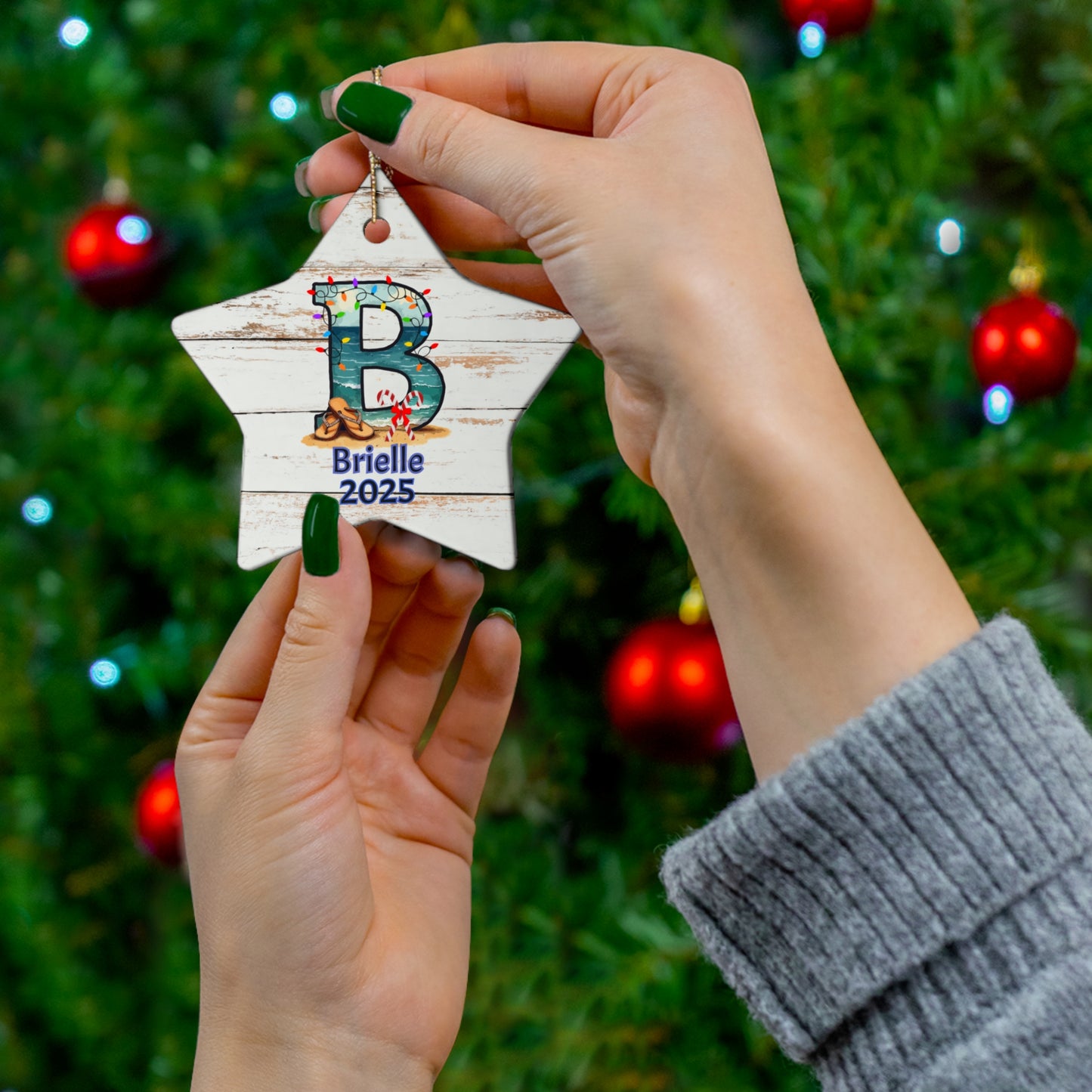 Hand holding a star-shaped ornament with 'B' and 'Brielle 2025' against a Christmas tree background.