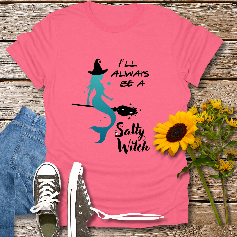 Pink t-shirt with mermaid graphic and text 'I'll always be a salty witch' on a wooden surface with jeans, shoes, and sunflowers.