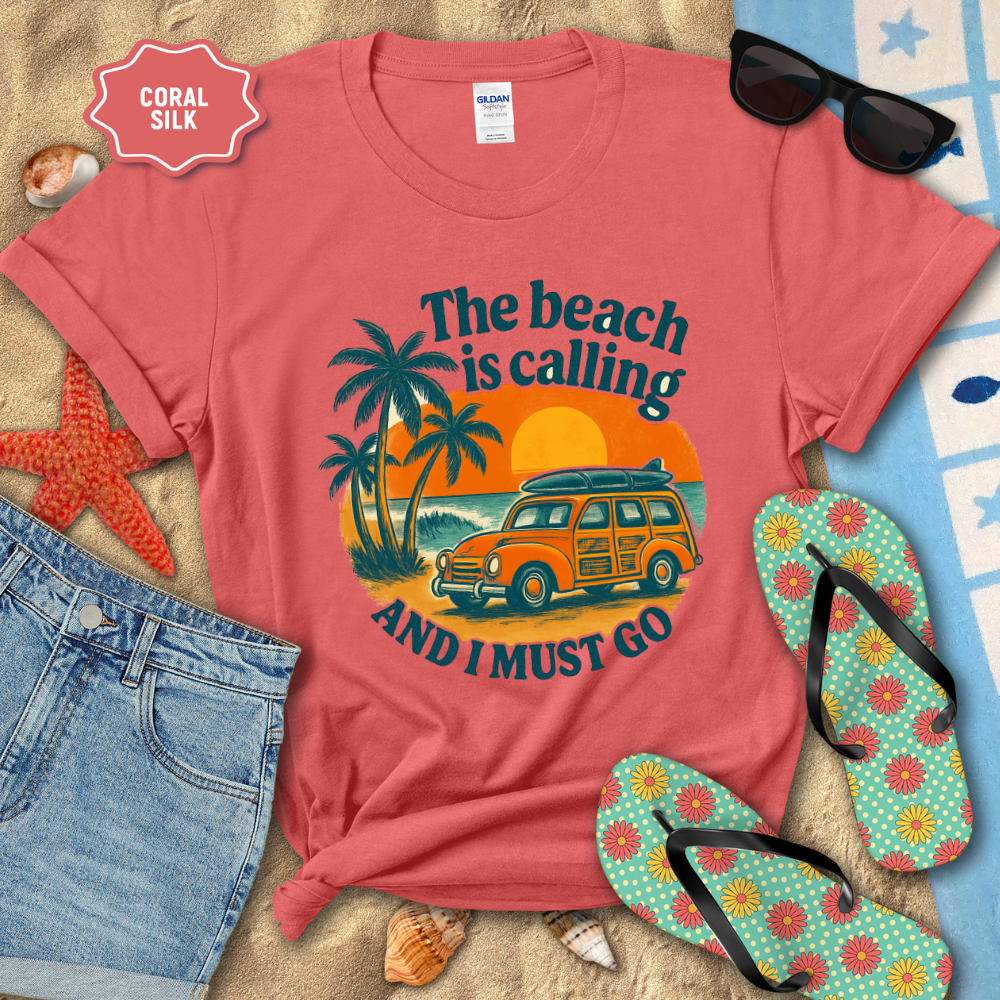 Coral t-shirt with beach-themed design on sand with sunglasses, flip-flops, and jeans.