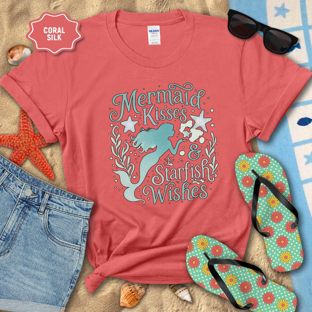 Coral t-shirt with mermaid design and beach accessories on sand