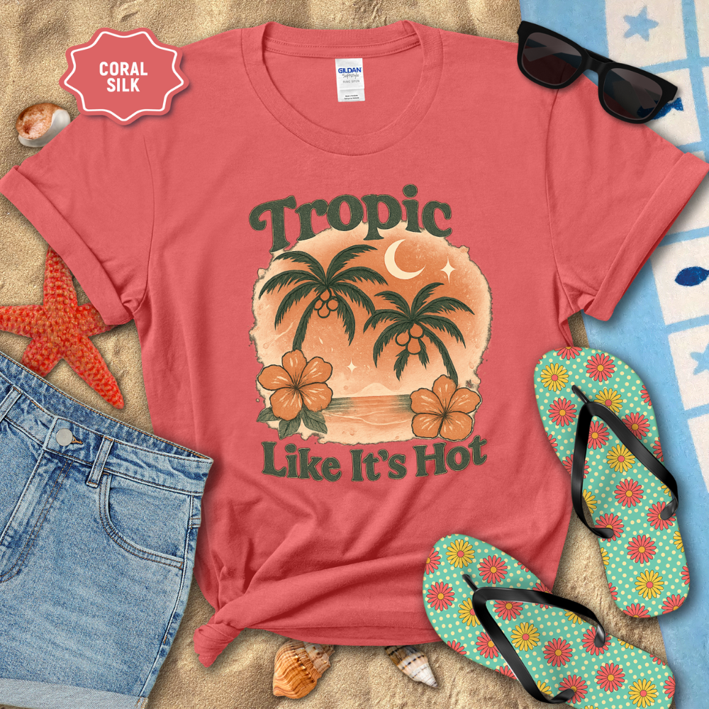 Red t-shirt with tropical design and text, sunglasses, flip-flops, and beach items on sand.