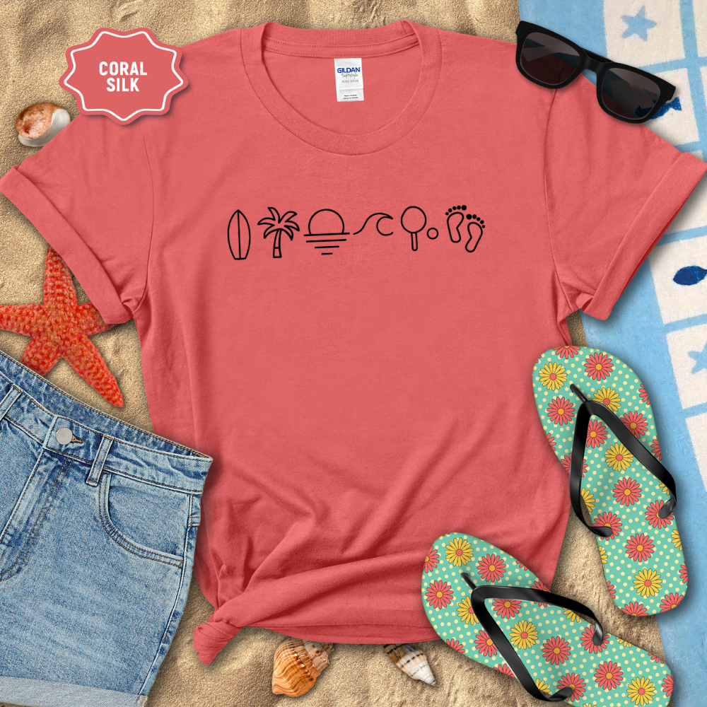 Coral t-shirt with 'make waves' design on a sandy surface with beach accessories.