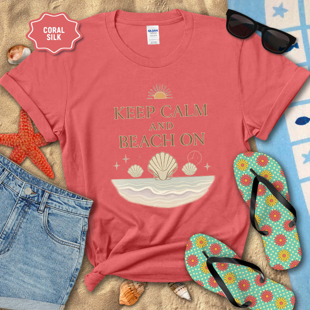 Coral t-shirt with 'Keep Calm and Beach On' design on sand with sunglasses, flip-flops, and beach accessories.