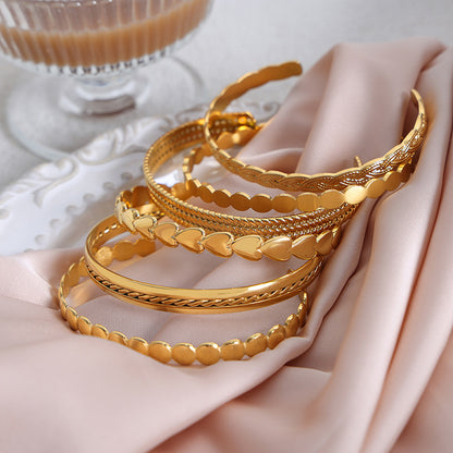 Three gold bracelets on a pink fabric with a blurred glass of coffee in the background