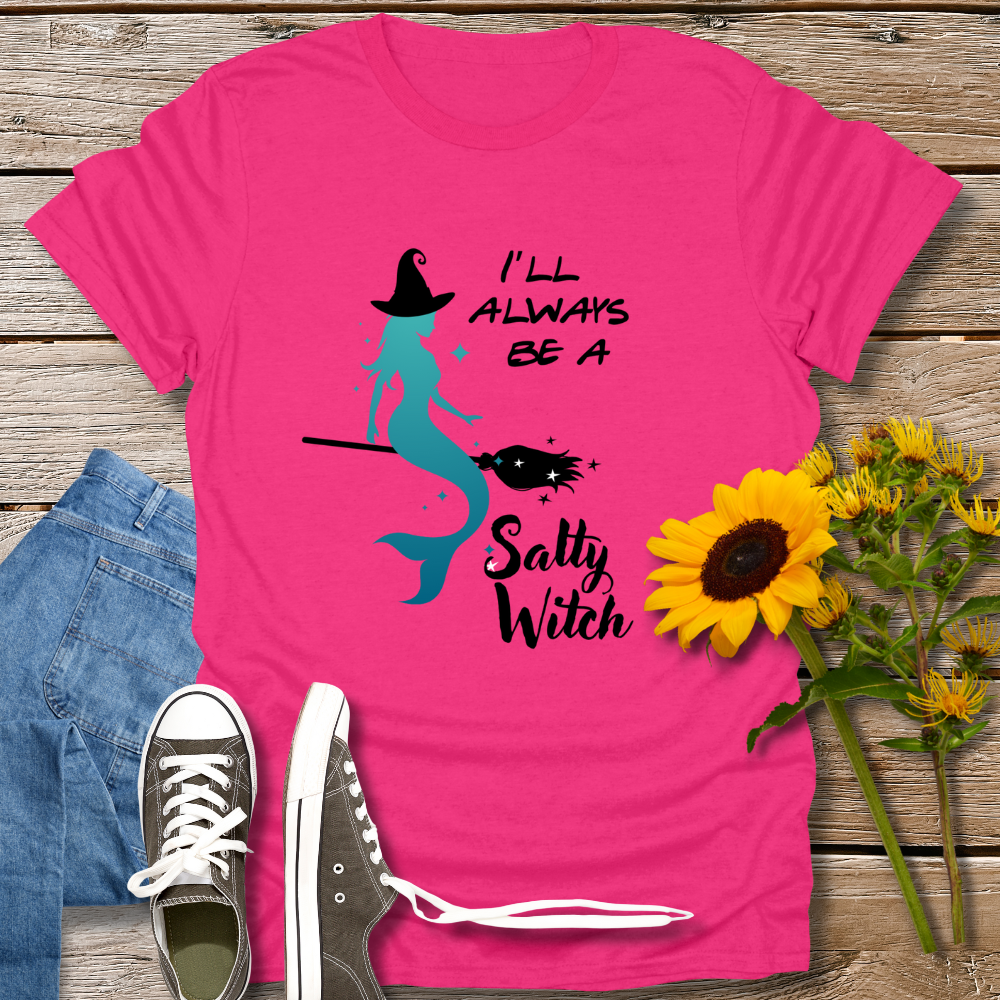 Pink t-shirt with mermaid graphic and text on a wooden surface with jeans and sunflowers.