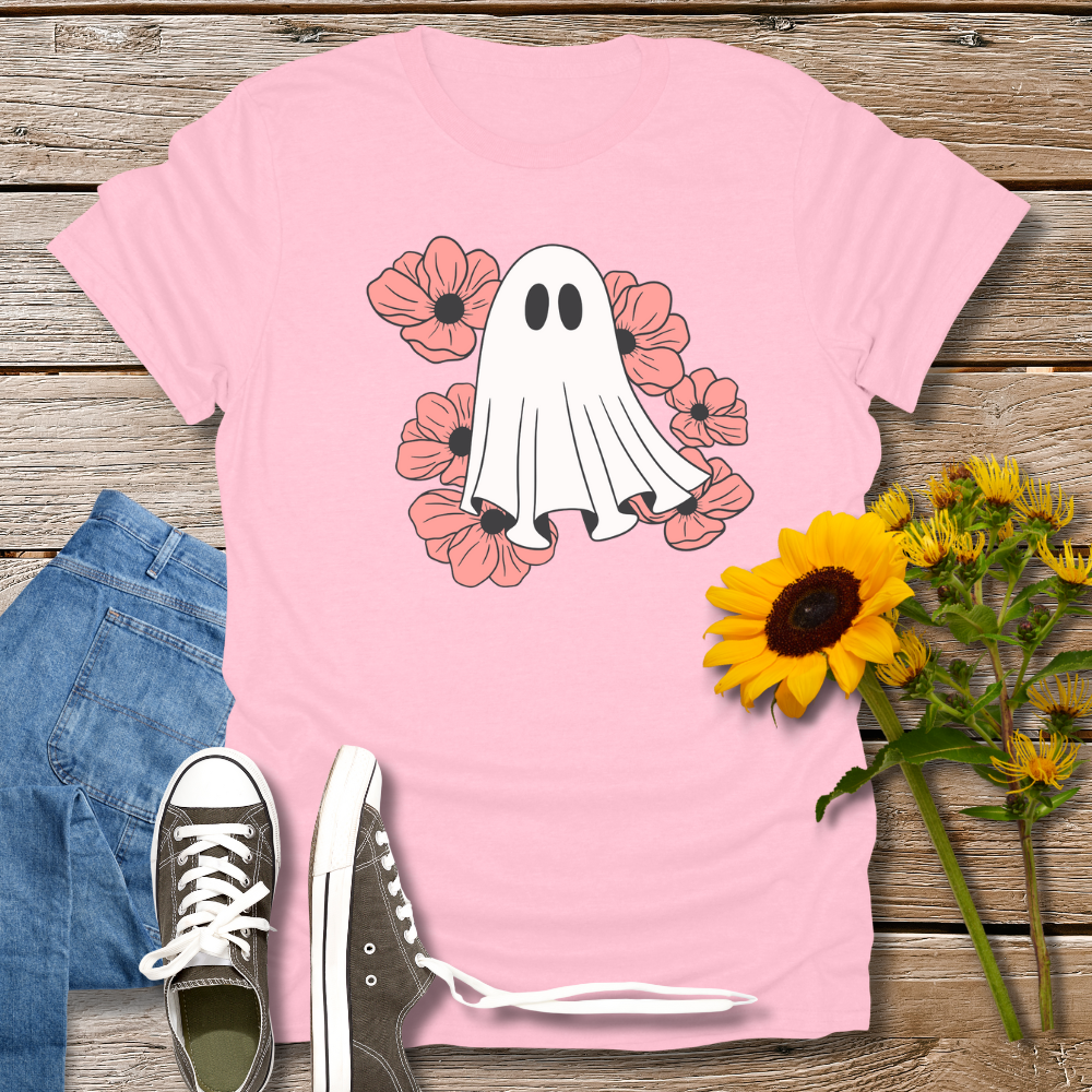 Pink t-shirt with ghost and flower design on a wooden surface with jeans and sneakers.