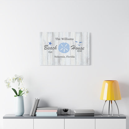 Decorative wall art with 'Beach House' text on a white wall above a shelf with books and a lamp.