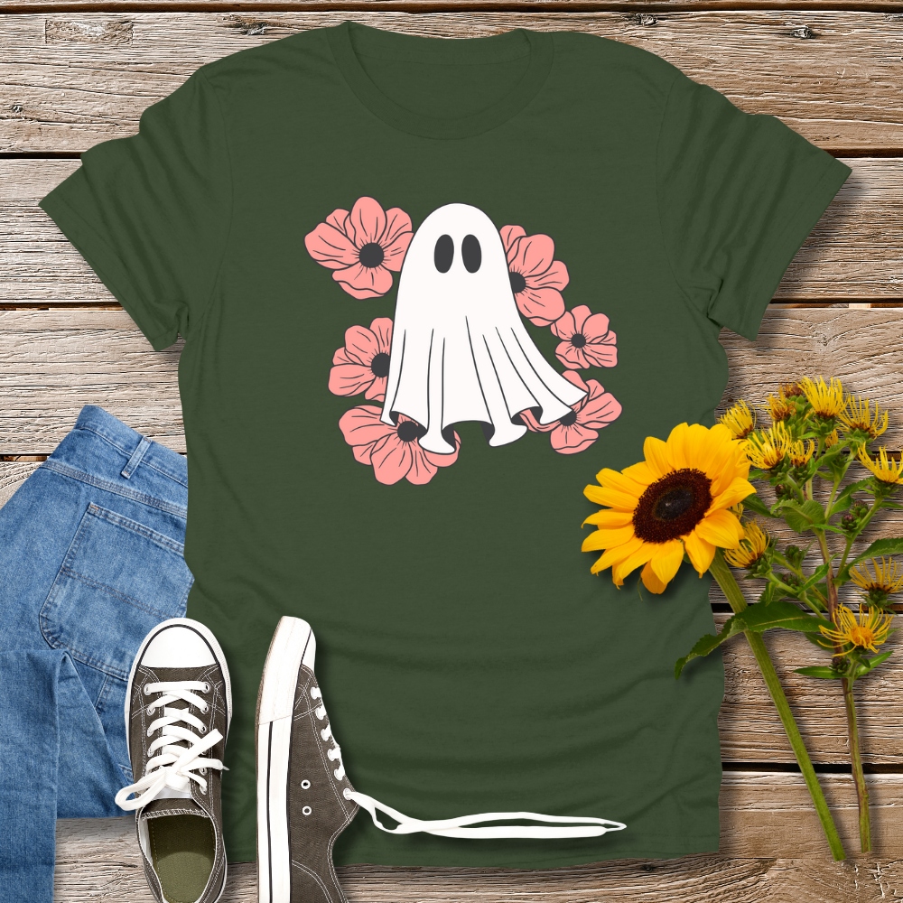 Green t-shirt with ghost and flowers design on a wooden surface with jeans and sunflowers.