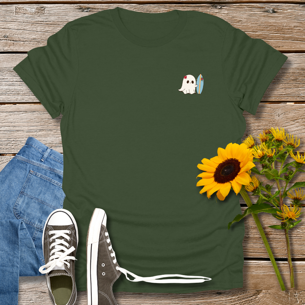 Green t-shirt with a ghost holding a surfboard design, paired with jeans and sneakers on a wooden surface.