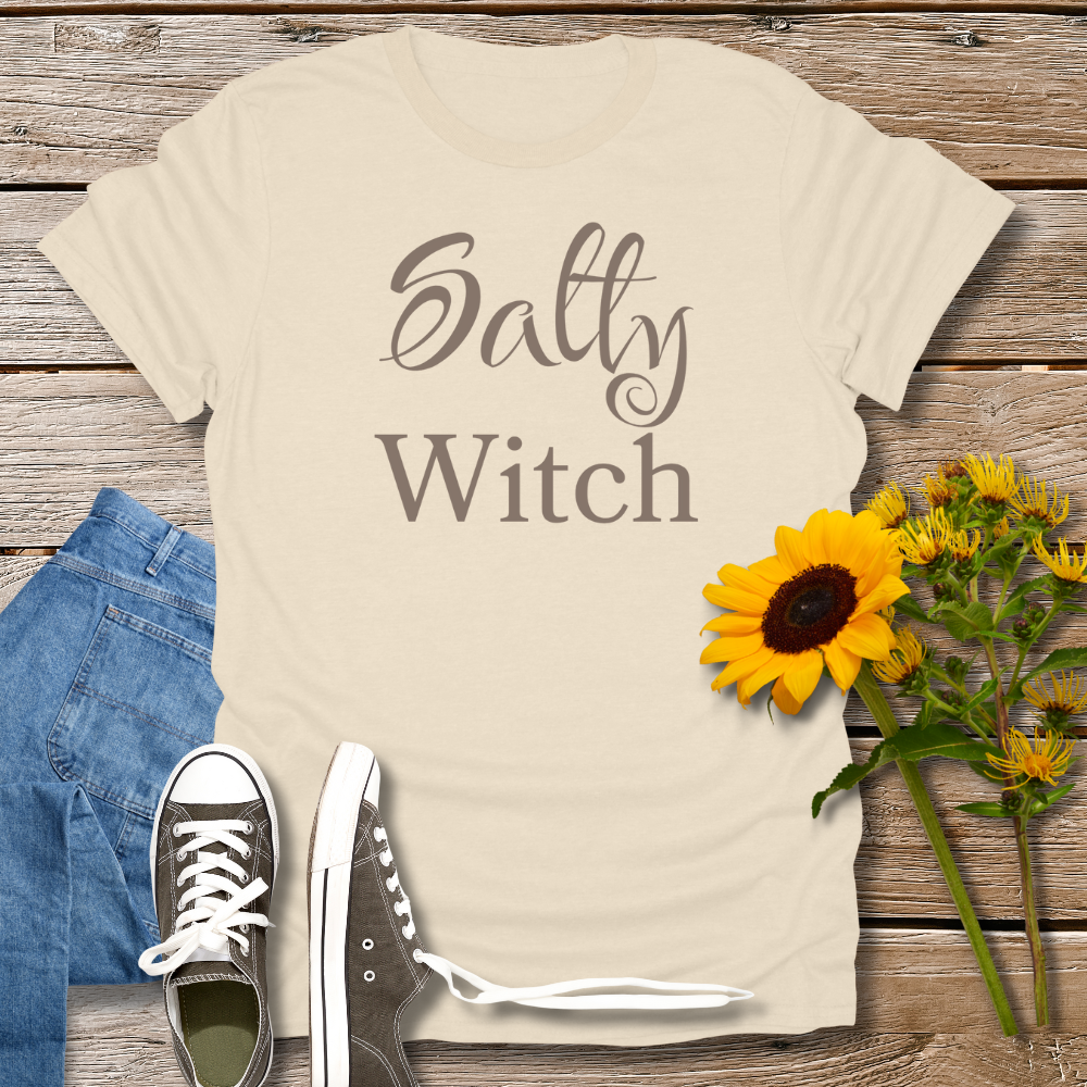 Beige t-shirt with 'Salty Witch' text, blue jeans, black sneakers, and sunflowers on a wooden surface