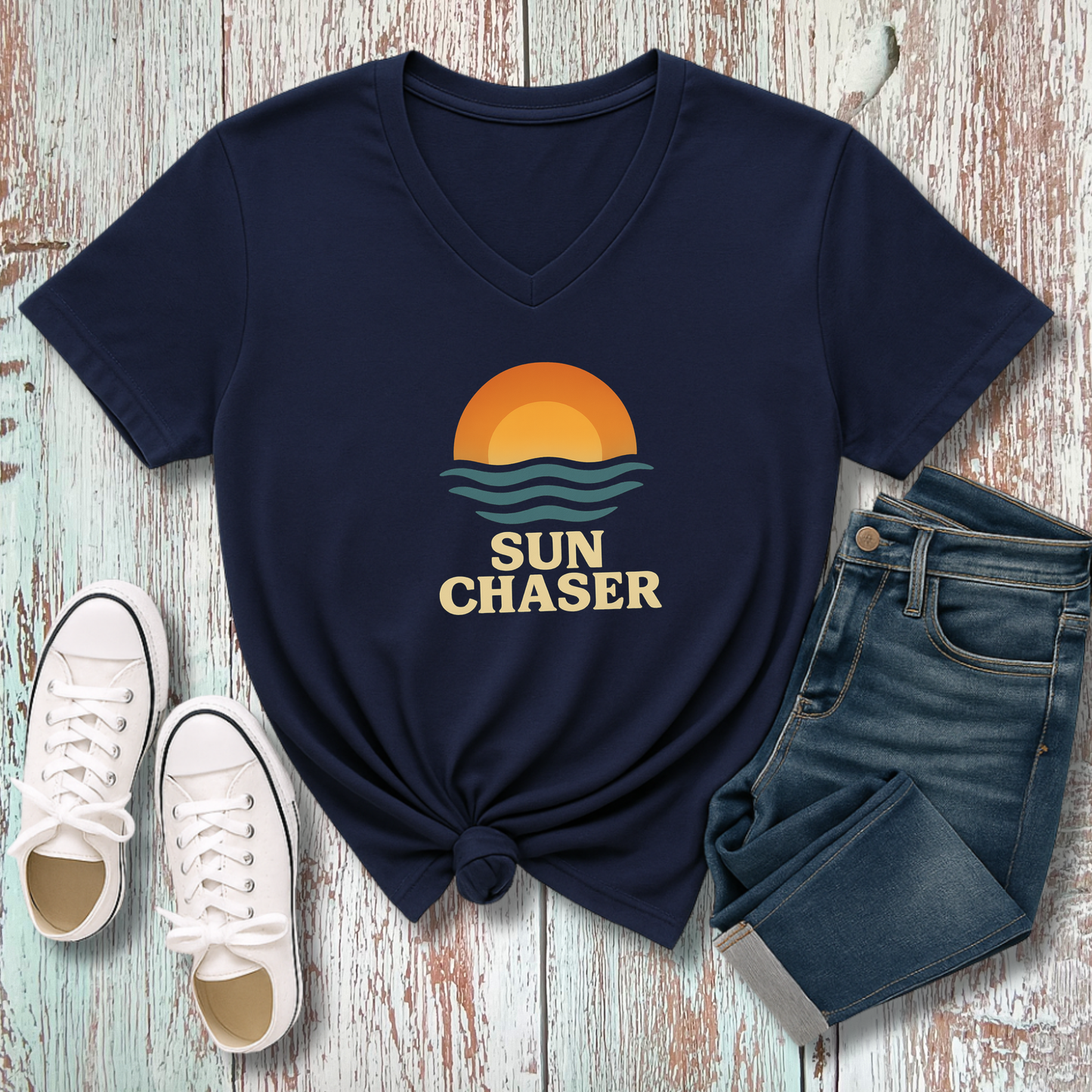 Navy blue t-shirt with 'Sun Chaser' design, white sneakers, and jeans on a wooden surface