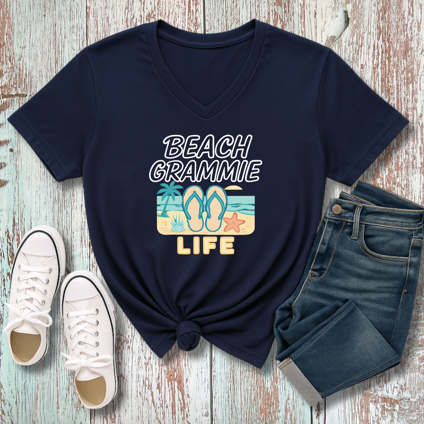 Navy blue t-shirt with 'Beach Grammie Life' design, white sneakers, and denim shorts on a wooden surface.