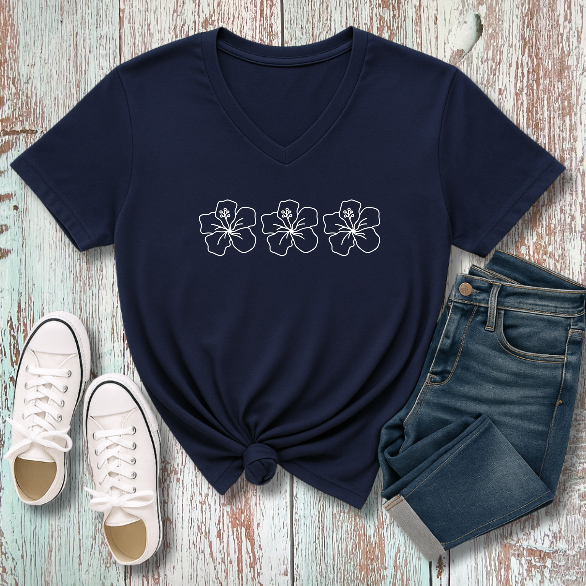 Navy blue t-shirt with floral design, white sneakers, and jeans on a wooden surface