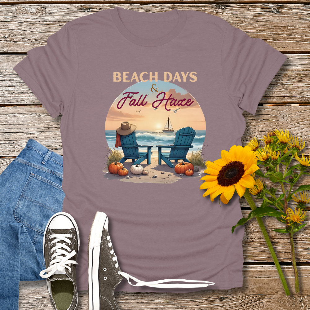 Purple t-shirt with beach and fall design on a wooden surface with jeans, sneakers, and sunflowers.