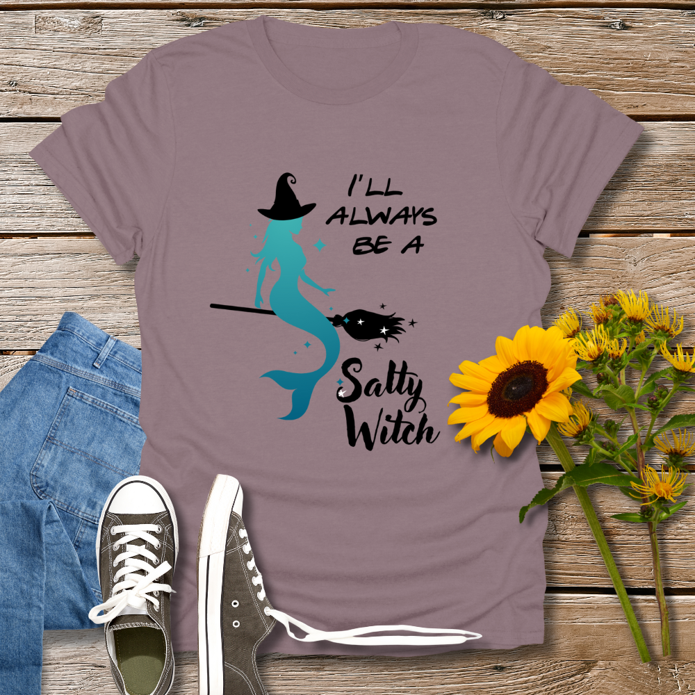 Purple t-shirt with mermaid and text design on a wooden surface with jeans, shoes, and sunflowers.