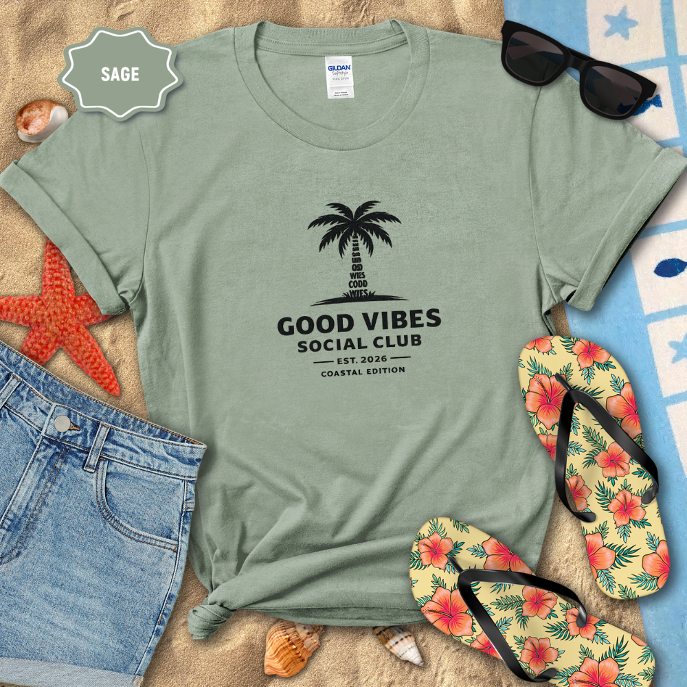 Sage green t-shirt with 'Good Vibes Social Club' design on a beach setting with sunglasses, flip-flops, and starfish.