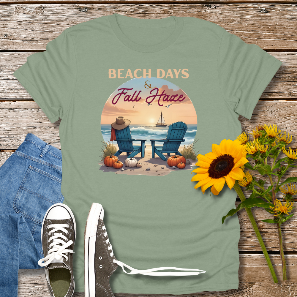Green t-shirt with beach and fall design on a wooden surface with sunflowers and jeans.