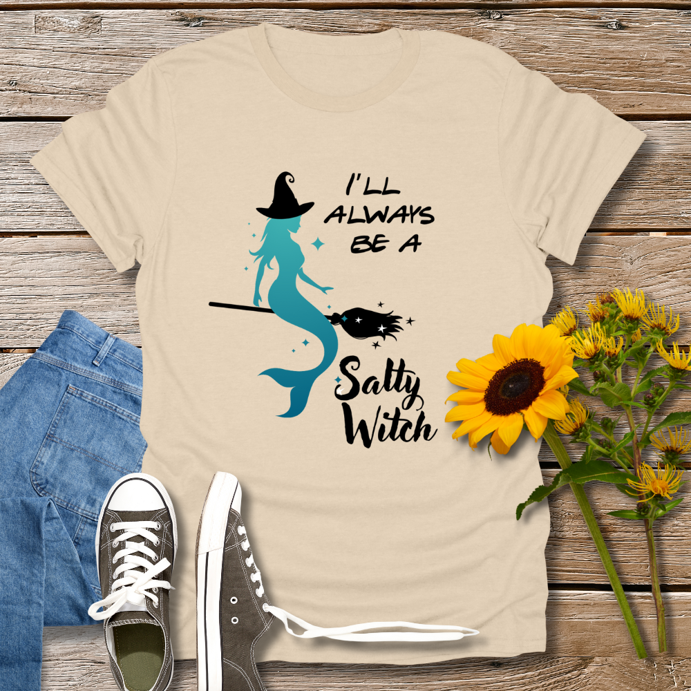 Beige t-shirt with mermaid and text design on a wooden surface with jeans, shoes, and sunflowers.