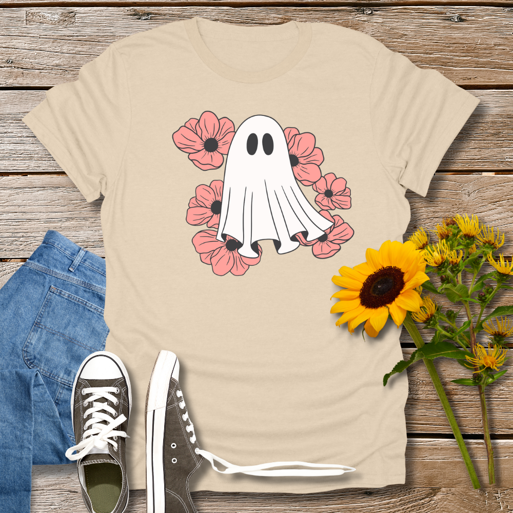 Beige t-shirt with ghost and flower design on a wooden surface with jeans and sunflowers.