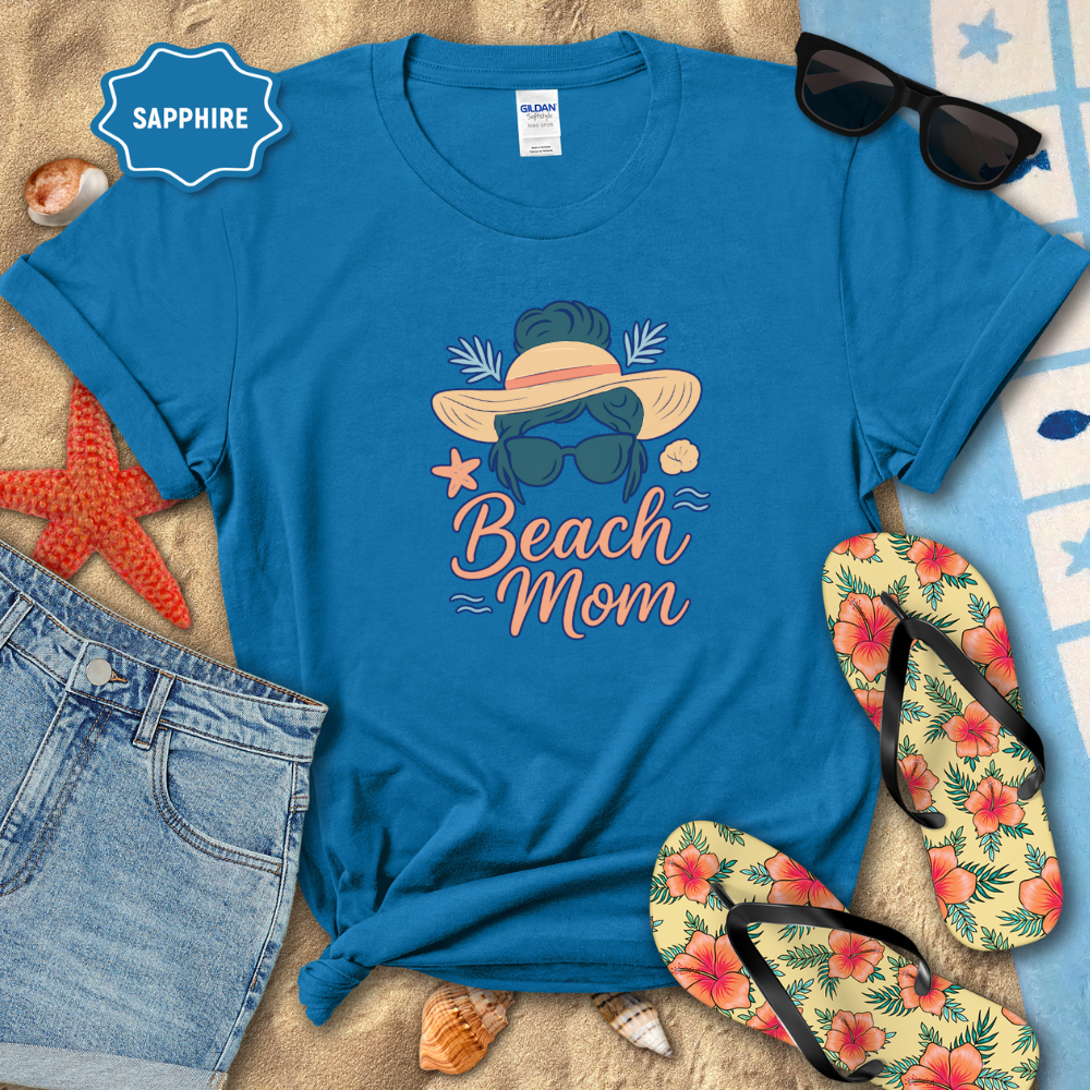 Blue t-shirt with 'Beach Mom' design on a sandy background with sunglasses, flip-flops, and beach accessories.