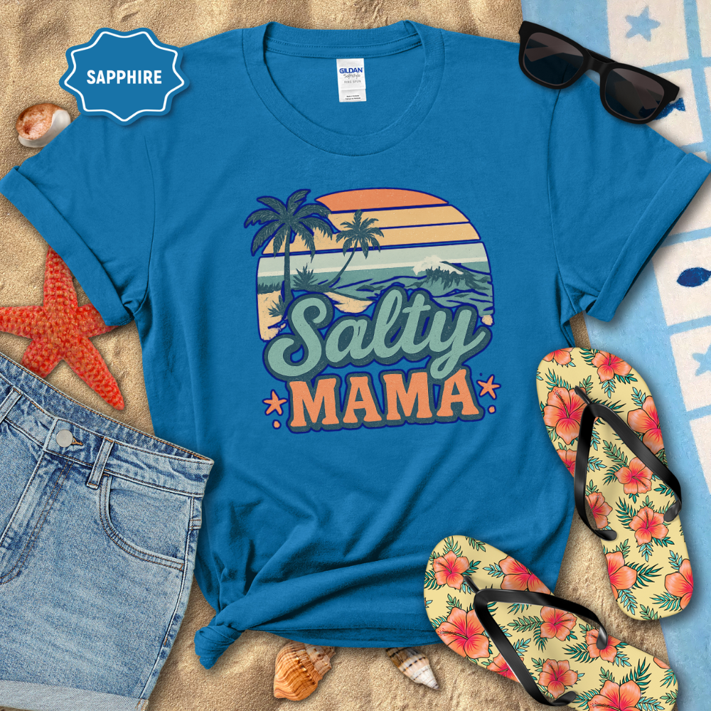 Blue t-shirt with 'Salty Mama' design on a beach setting with sunglasses, flip-flops, and denim shorts.