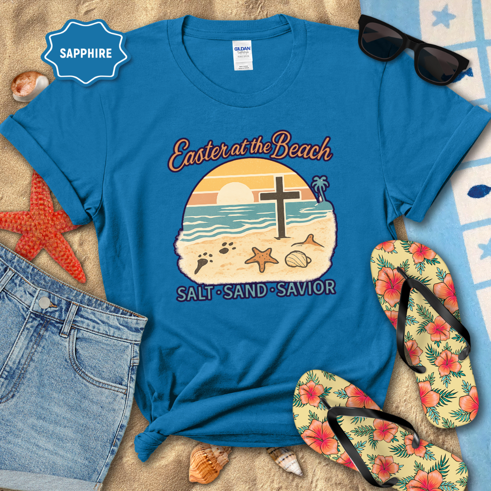 Blue t-shirt with 'Easter at the Beach' design on a sandy background with flip-flops and sunglasses.