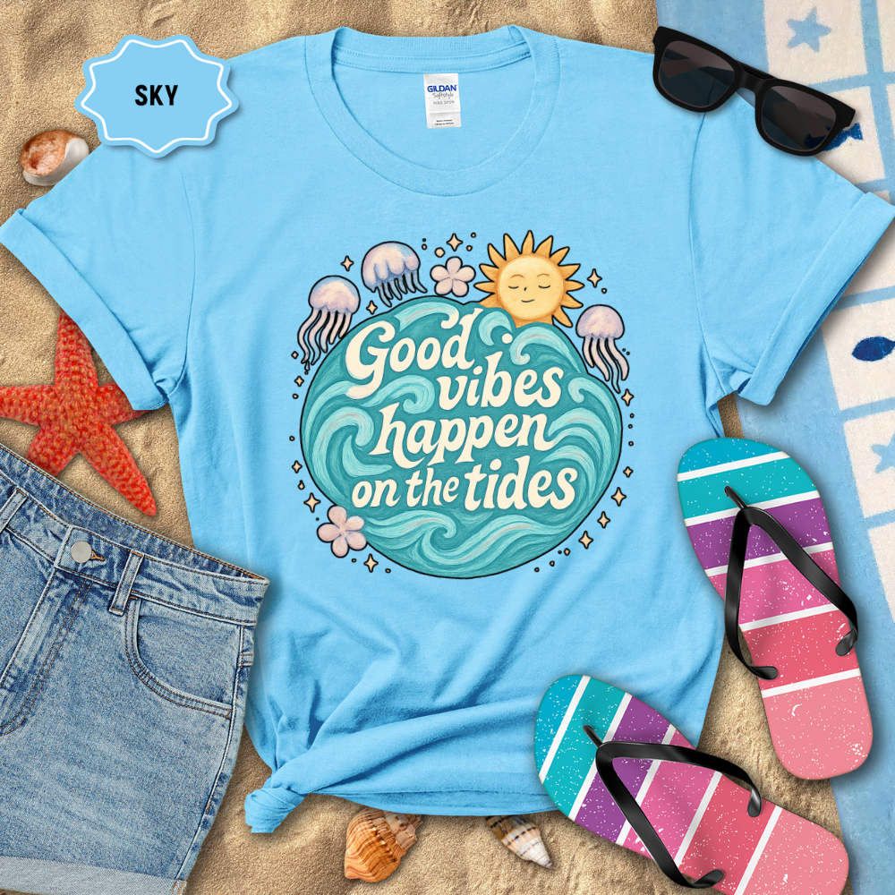 Light blue t-shirt with 'Good vibes happen on the tides' design, surrounded by beach accessories.