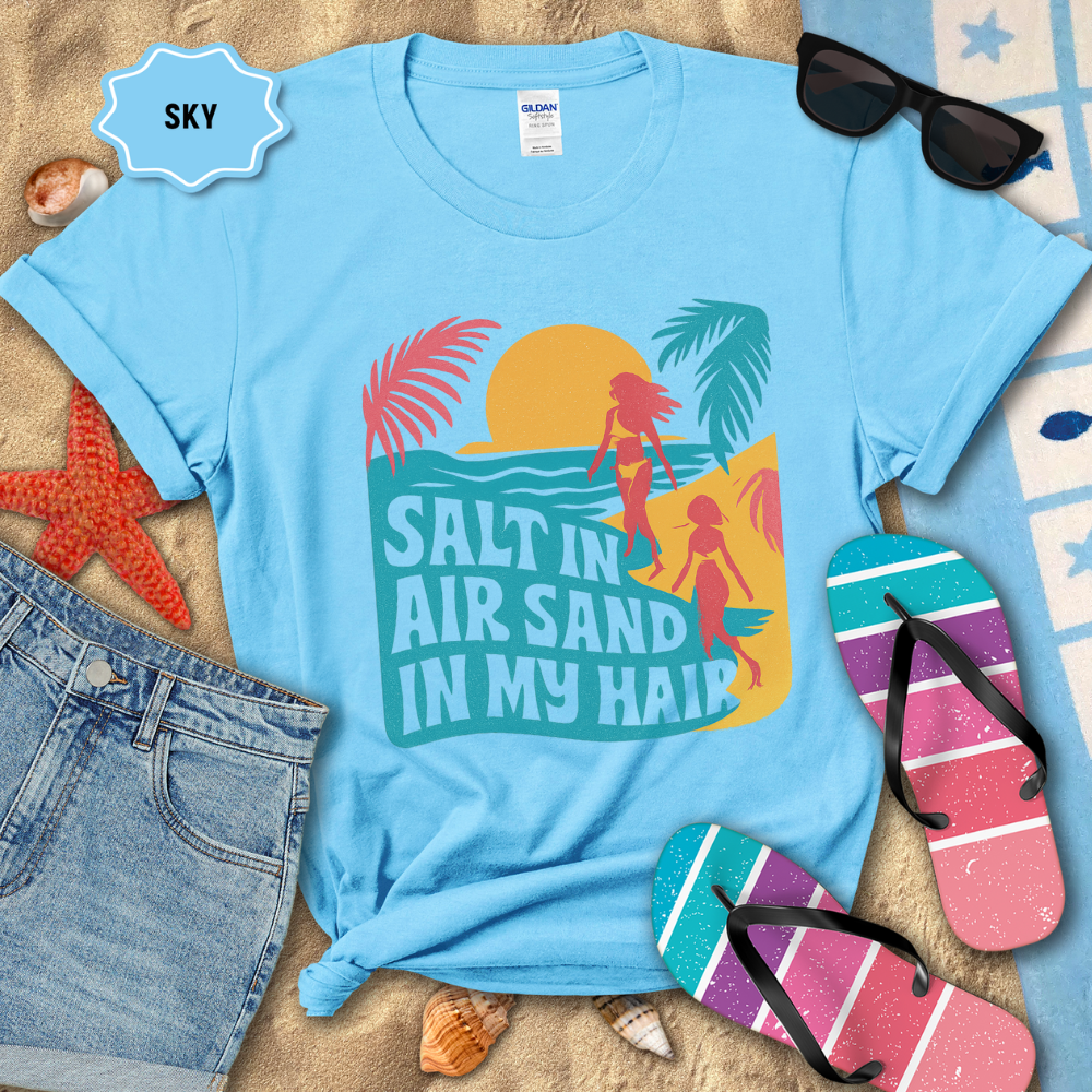 Light blue t-shirt with beach-themed design and accessories on sand