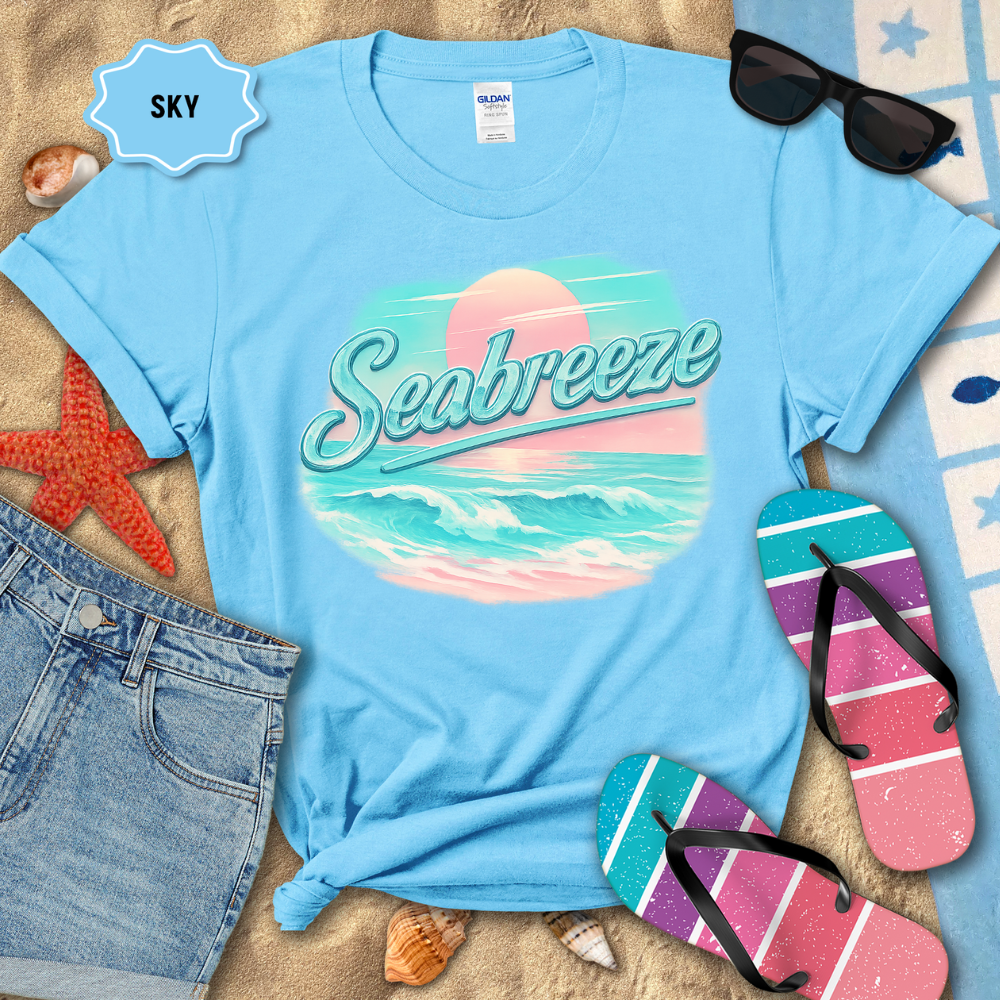 Blue t-shirt with 'Seabreeze' design on a sandy surface with beach accessories.