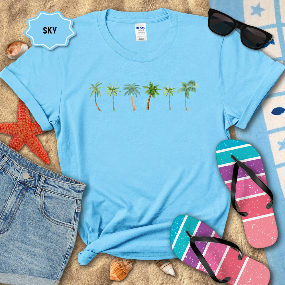 Blue t-shirt with palm tree design on a sandy surface with beach accessories.