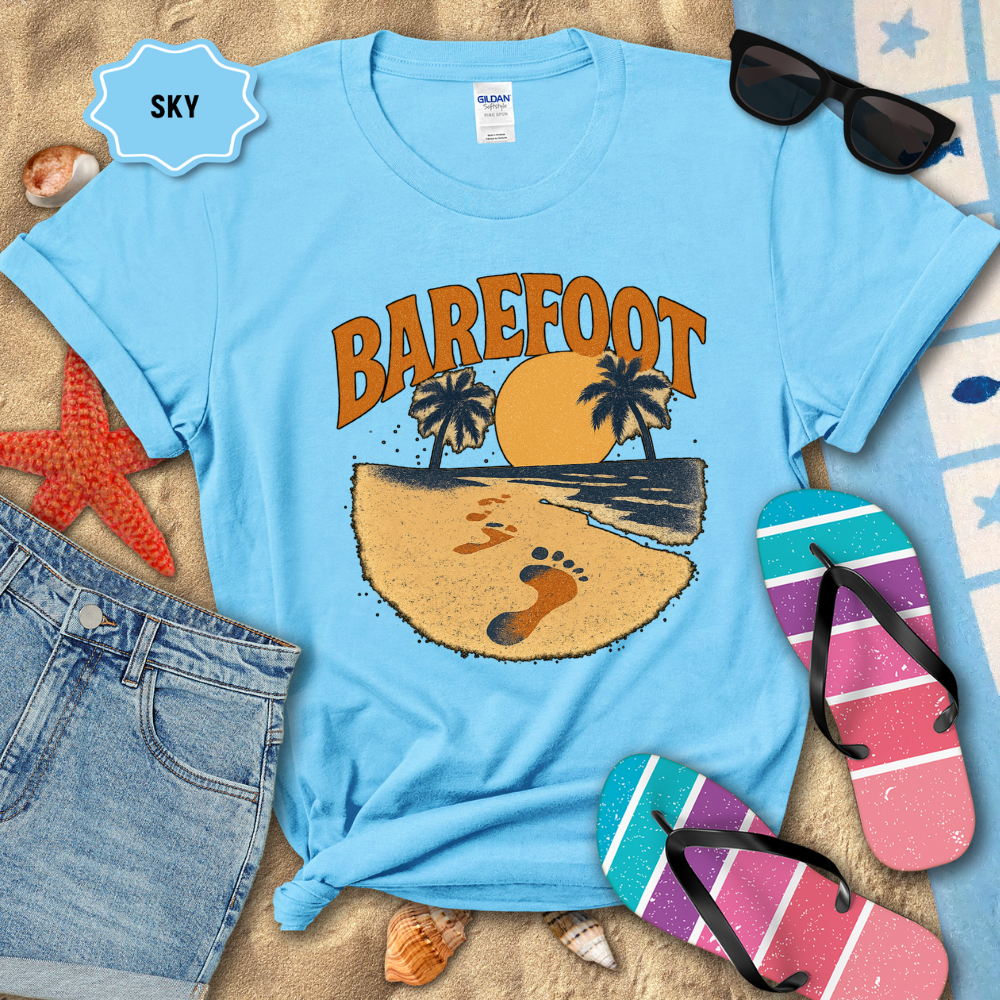 Light blue t-shirt with 'Barefoot' graphic design on a sandy background with beach accessories.