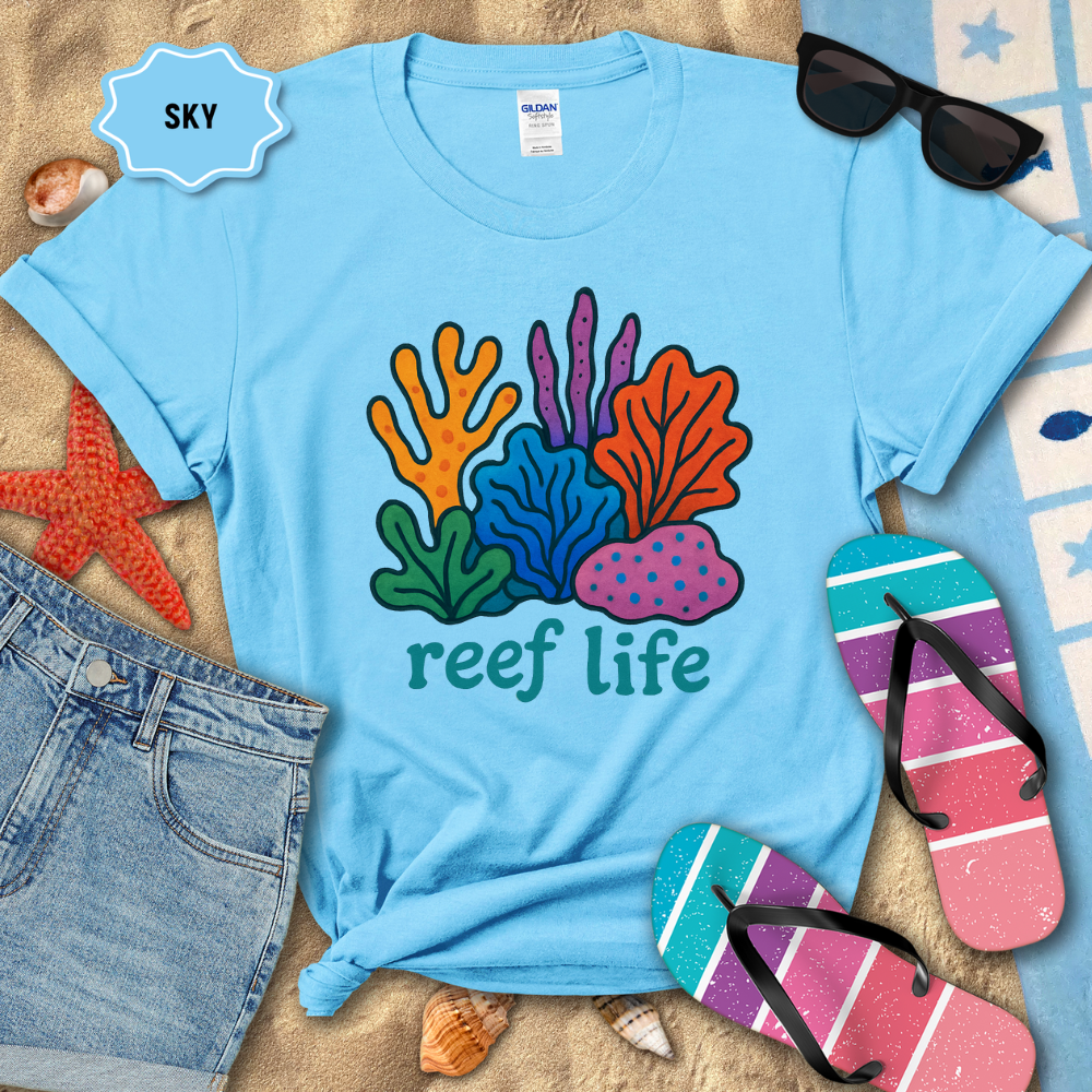 Light blue t-shirt with 'reef life' design on a sandy background with beach accessories.