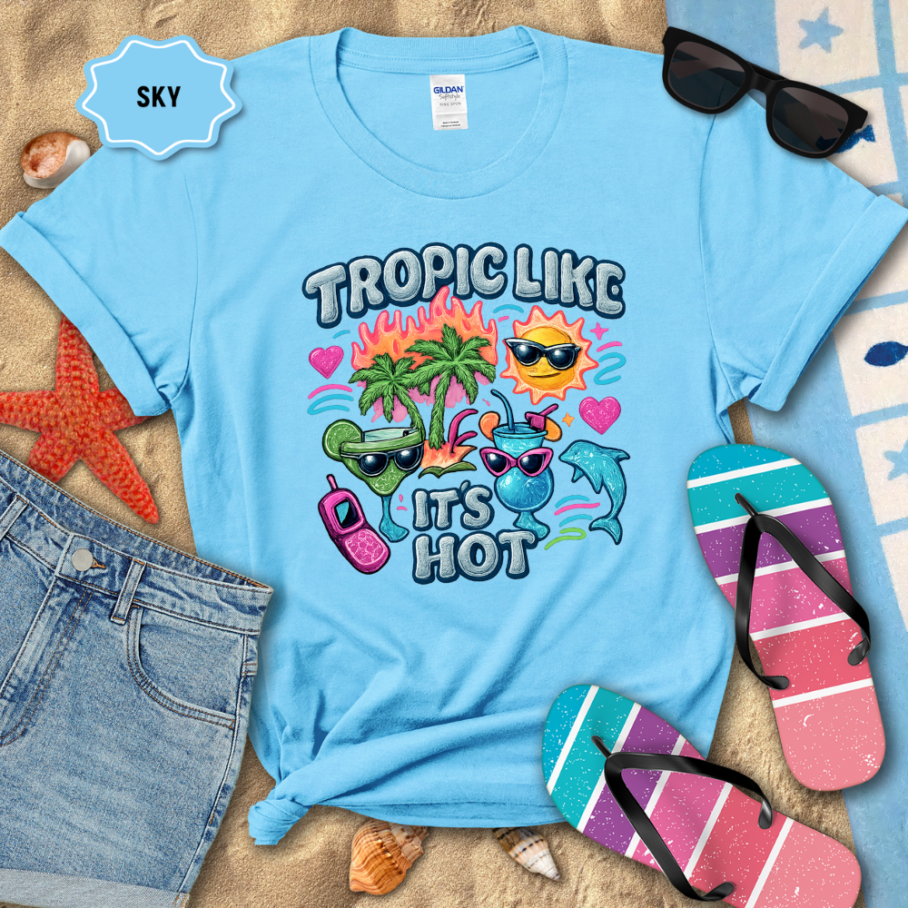 Light blue t-shirt with tropical-themed design on a sandy background with beach accessories.