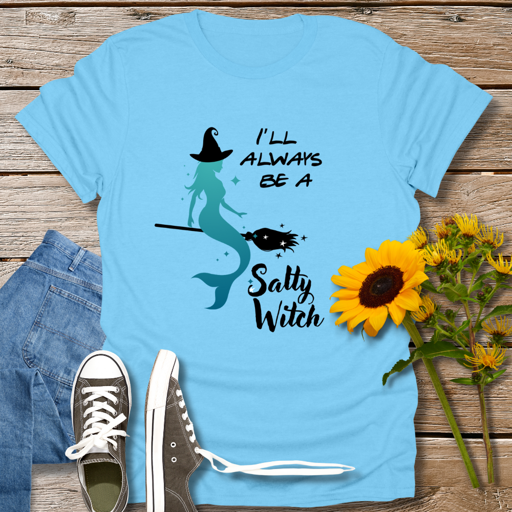Blue t-shirt with mermaid design and text on a wooden surface with jeans and sunflowers.