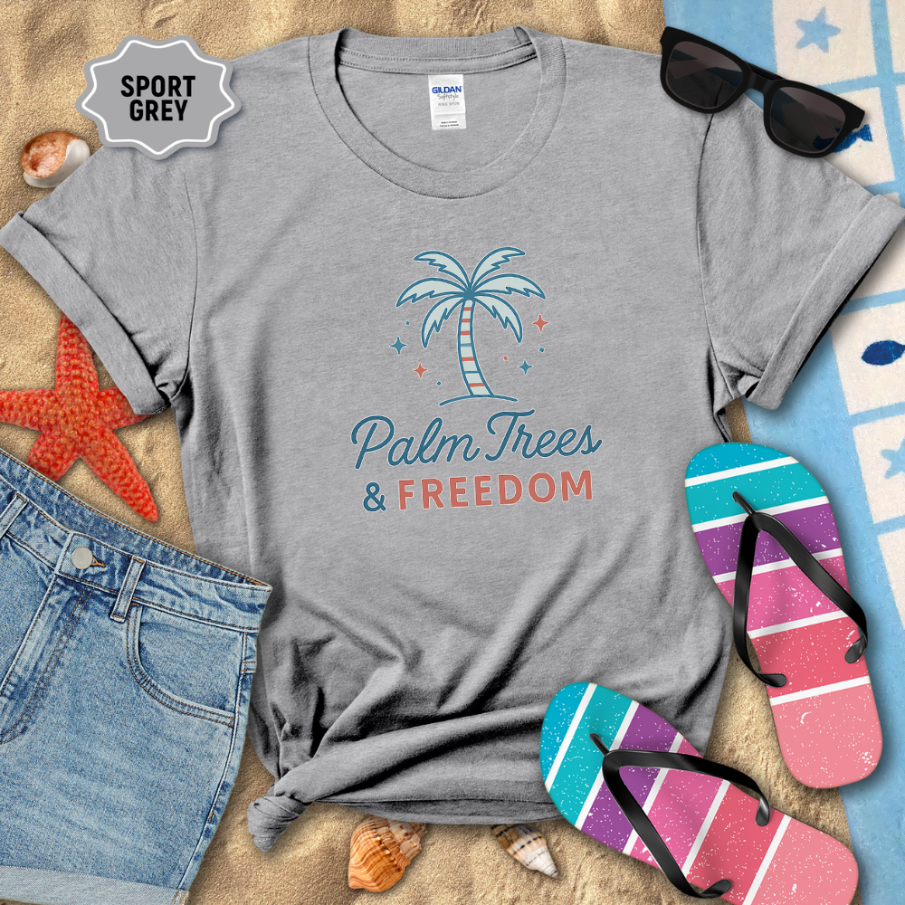 Gray t-shirt with 'Palm Trees & Freedom' design on a sandy background with beach accessories.