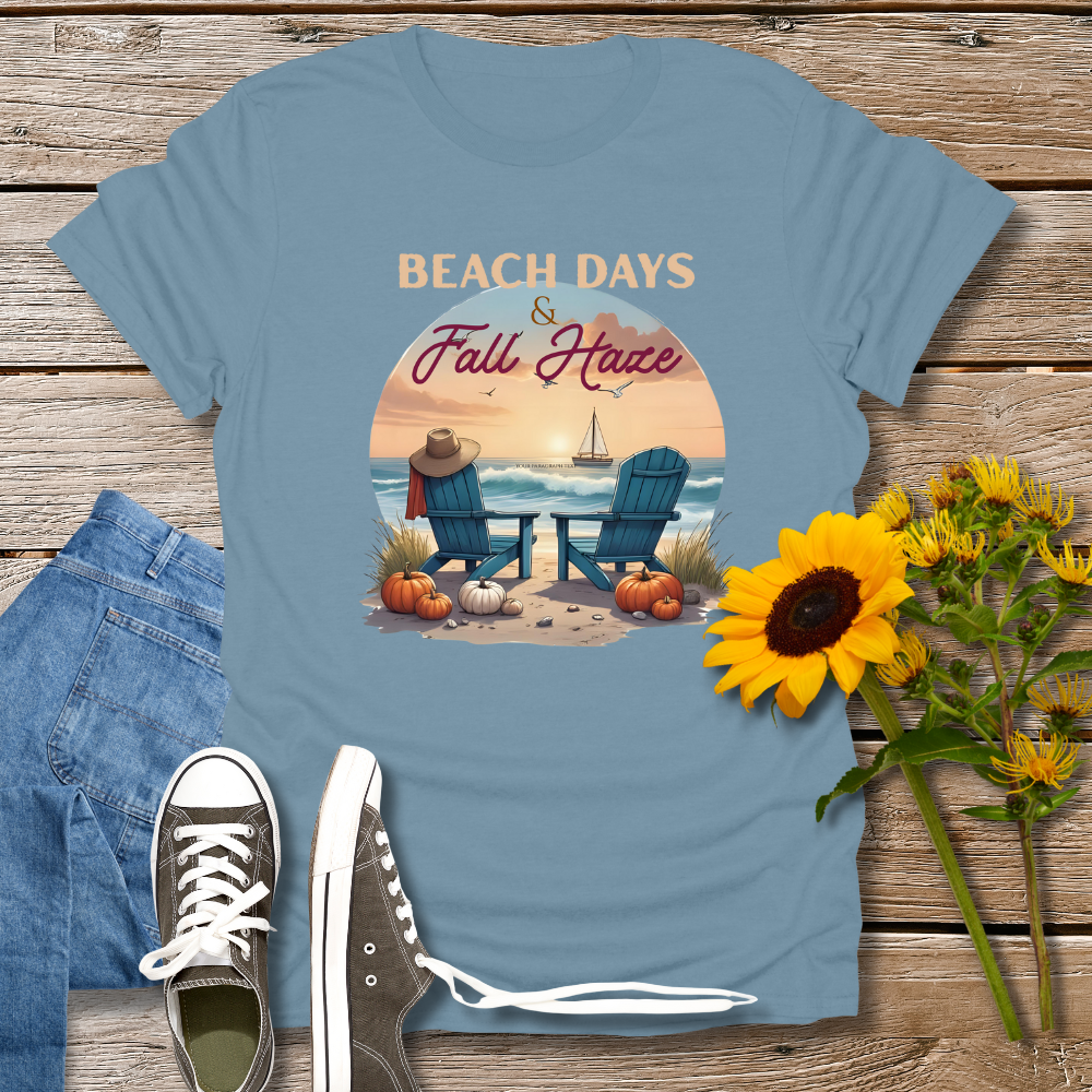 Blue t-shirt with beach and fall design on a wooden surface with sunflowers and jeans.