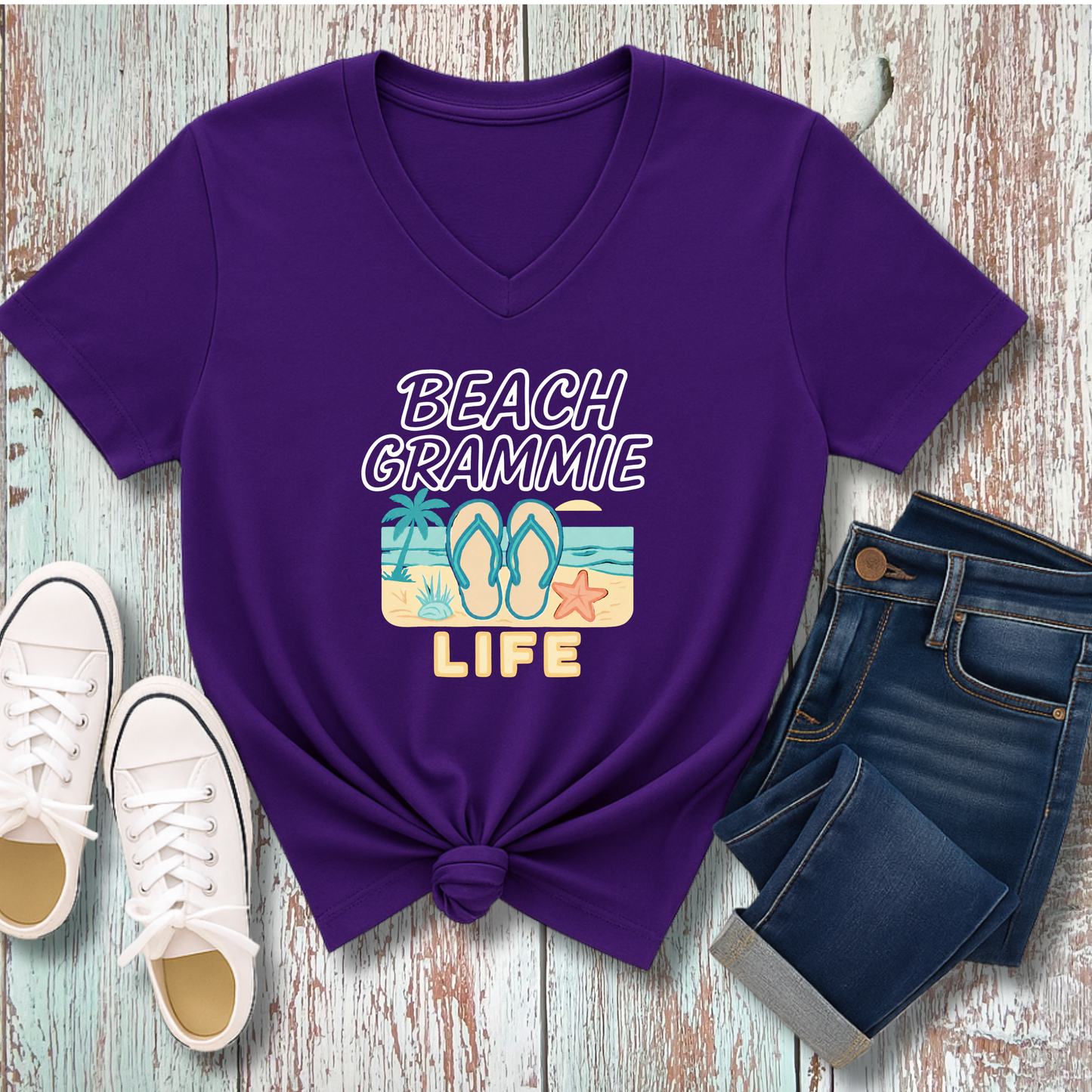 Purple t-shirt with 'Beach Grammie Life' design on a wooden surface with sneakers and jeans.