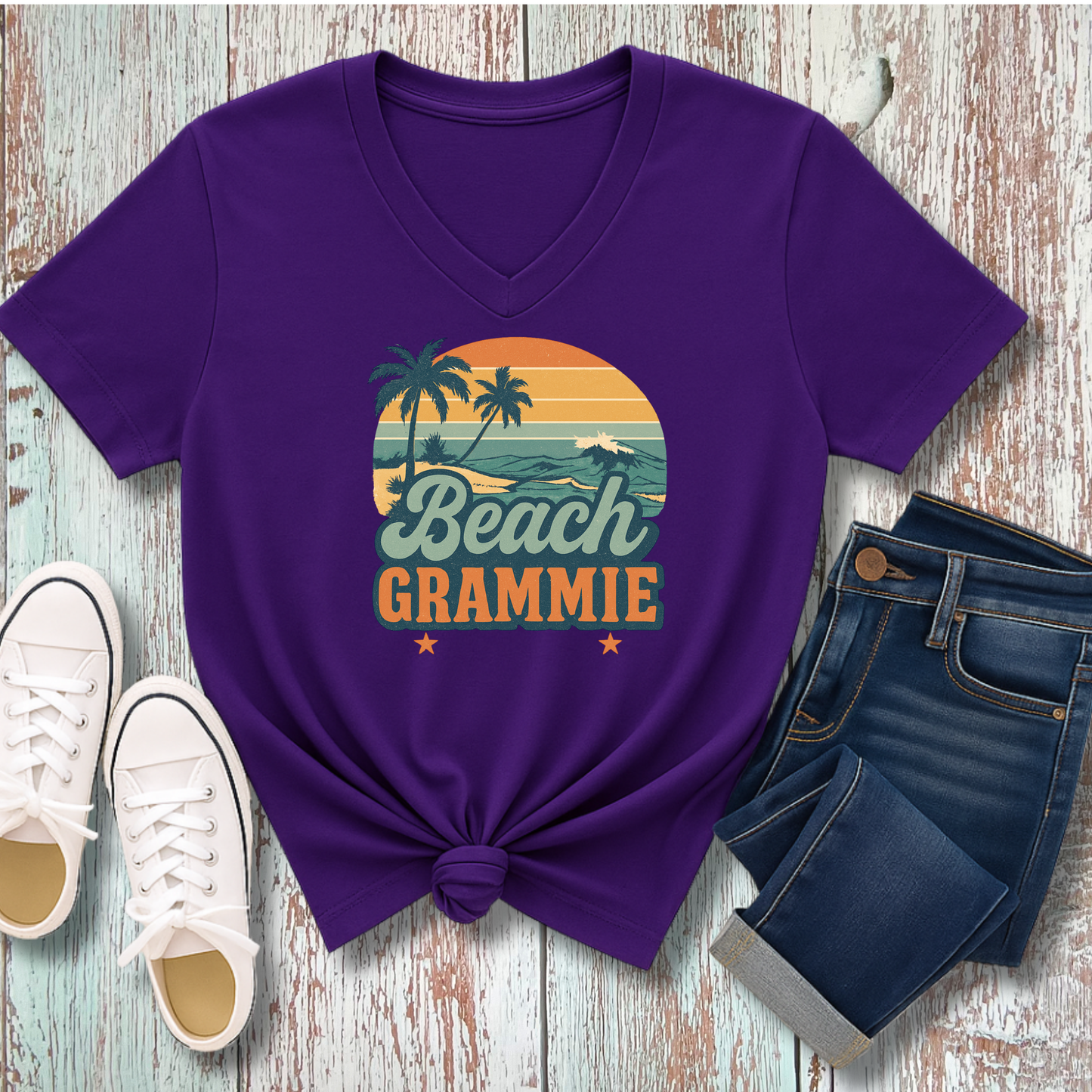 Purple t-shirt with 'Beach Grammie' design on a wooden surface with shoes and jeans.