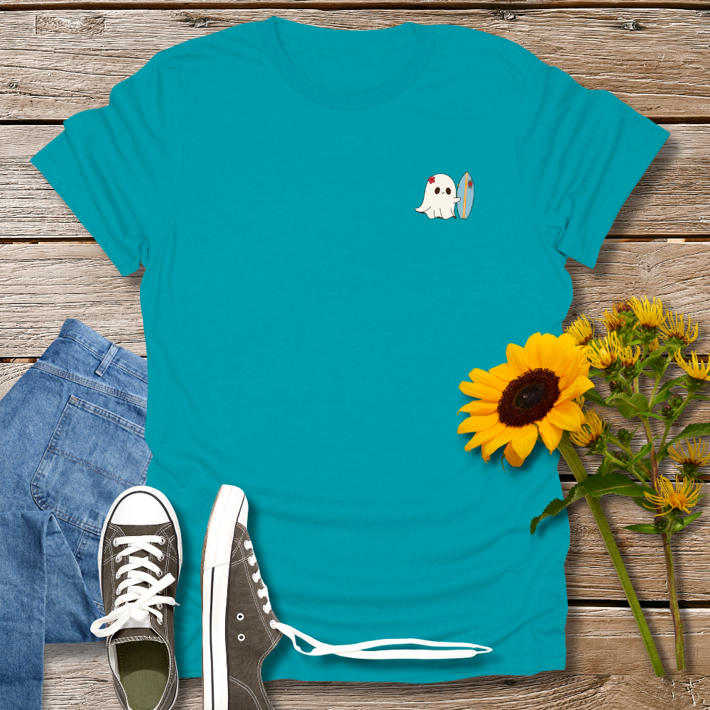 Teal t-shirt with ghost and surfboard design, paired with jeans and sneakers on a wooden surface.