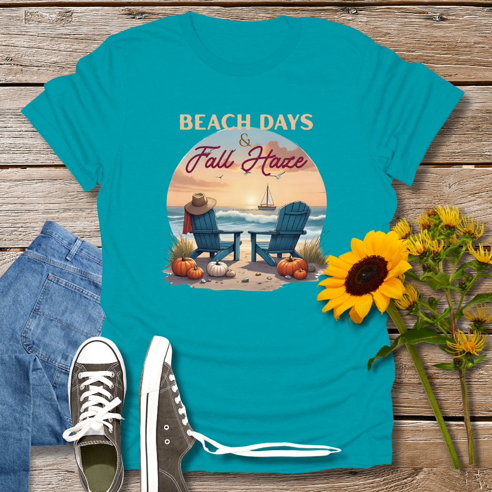 Blue t-shirt with beach and fall design on a wooden surface with sunflowers and jeans.
