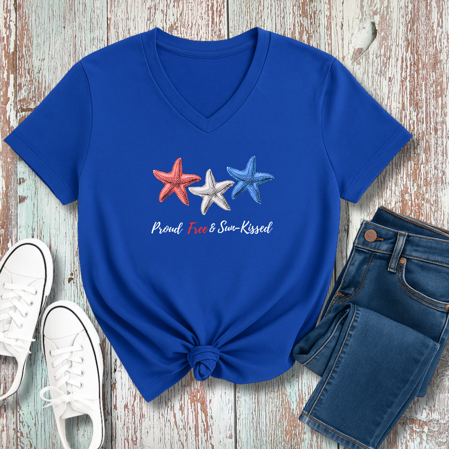 Blue t-shirt with star designs and text on a wooden surface with jeans and sneakers.